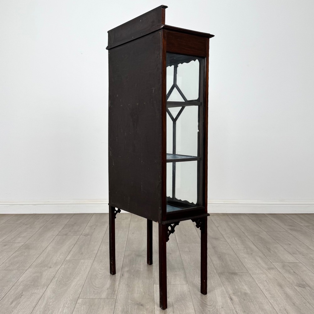 A slender Edwardian mahogany glazed display cabinet featuring astragal door bars and a fabric-lined interior raised on square legs. View VII