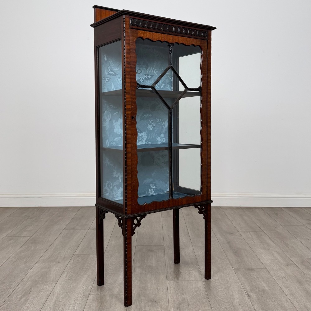 A slender Edwardian mahogany glazed display cabinet featuring astragal door bars and a fabric-lined interior raised on square legs. View IX