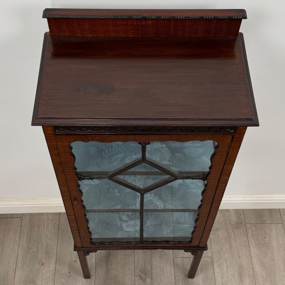 A slender Edwardian mahogany glazed display cabinet featuring astragal door bars and a fabric-lined interior raised on square legs. View X