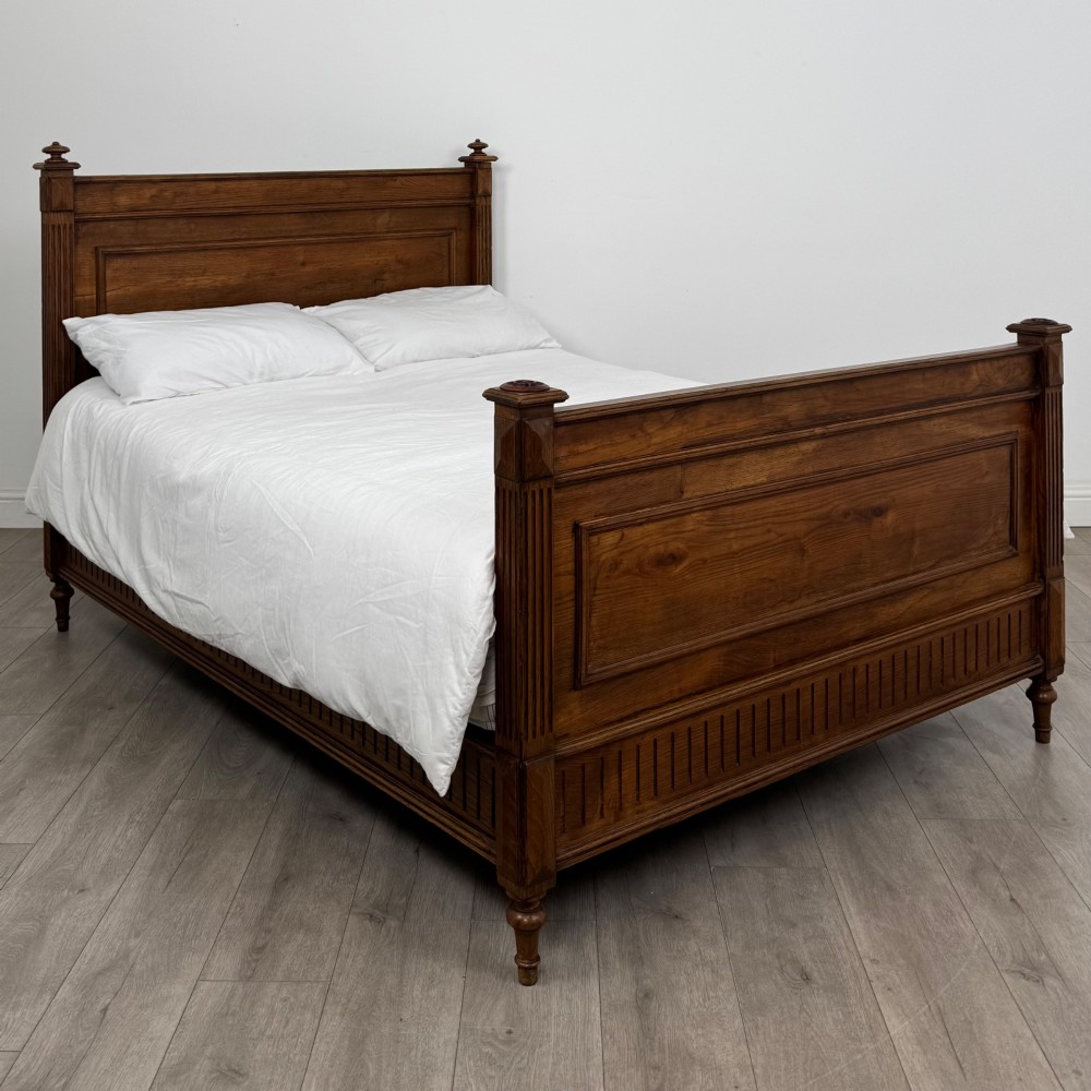 A 19th-century French oak double bed frame featuring a raised panelled headboard and footboard flanked by fluted posts with turned finials.