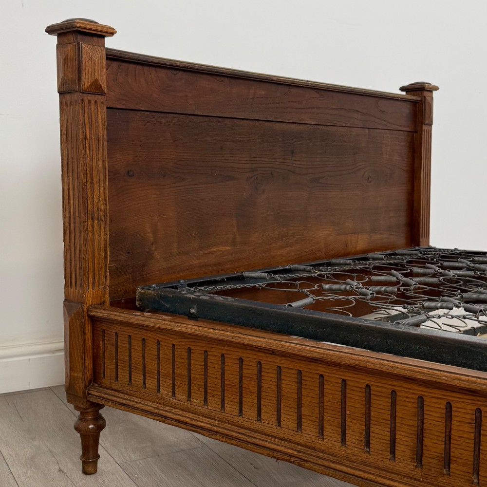 A 19th-century French oak double bed frame featuring a raised panelled headboard and footboard flanked by fluted posts with turned finials. View VI