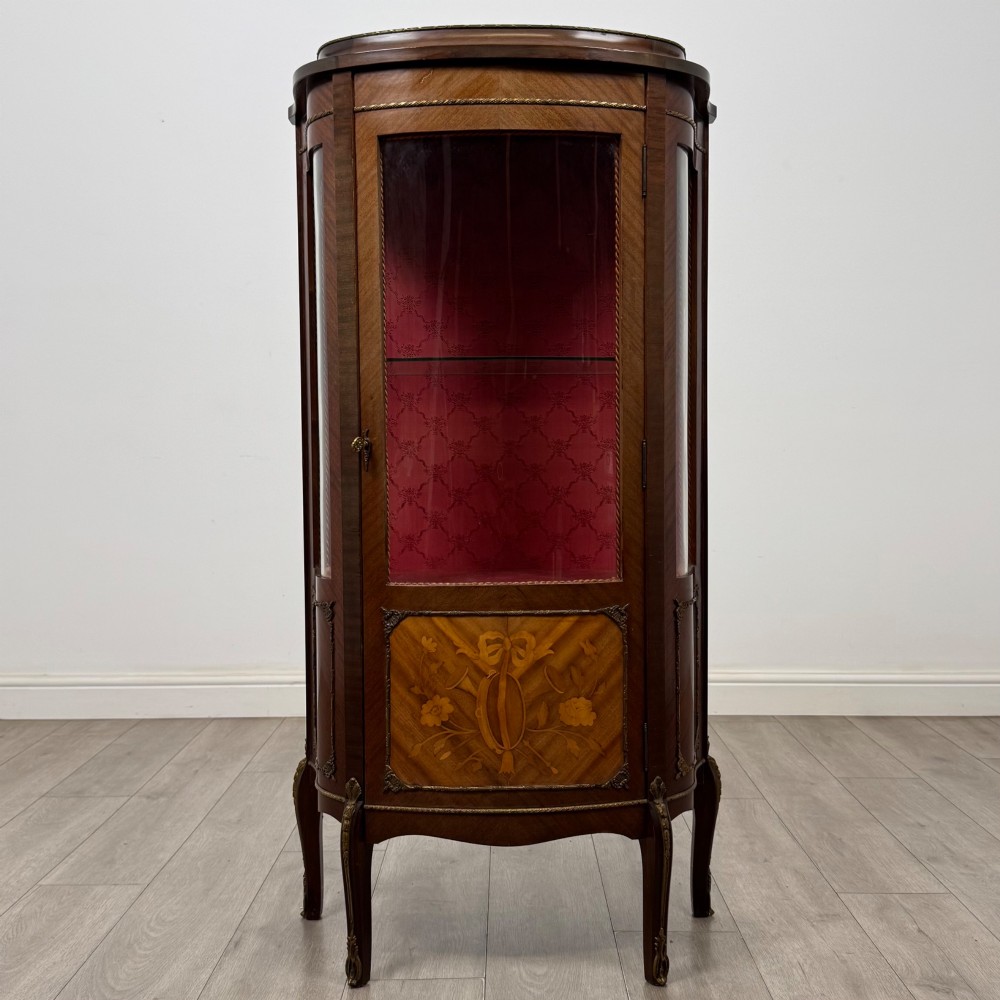 A French mahogany display vitrine featuring a curved glass door, red fabric interior lining, floral marquetry lower panel, and brass leg mounts.