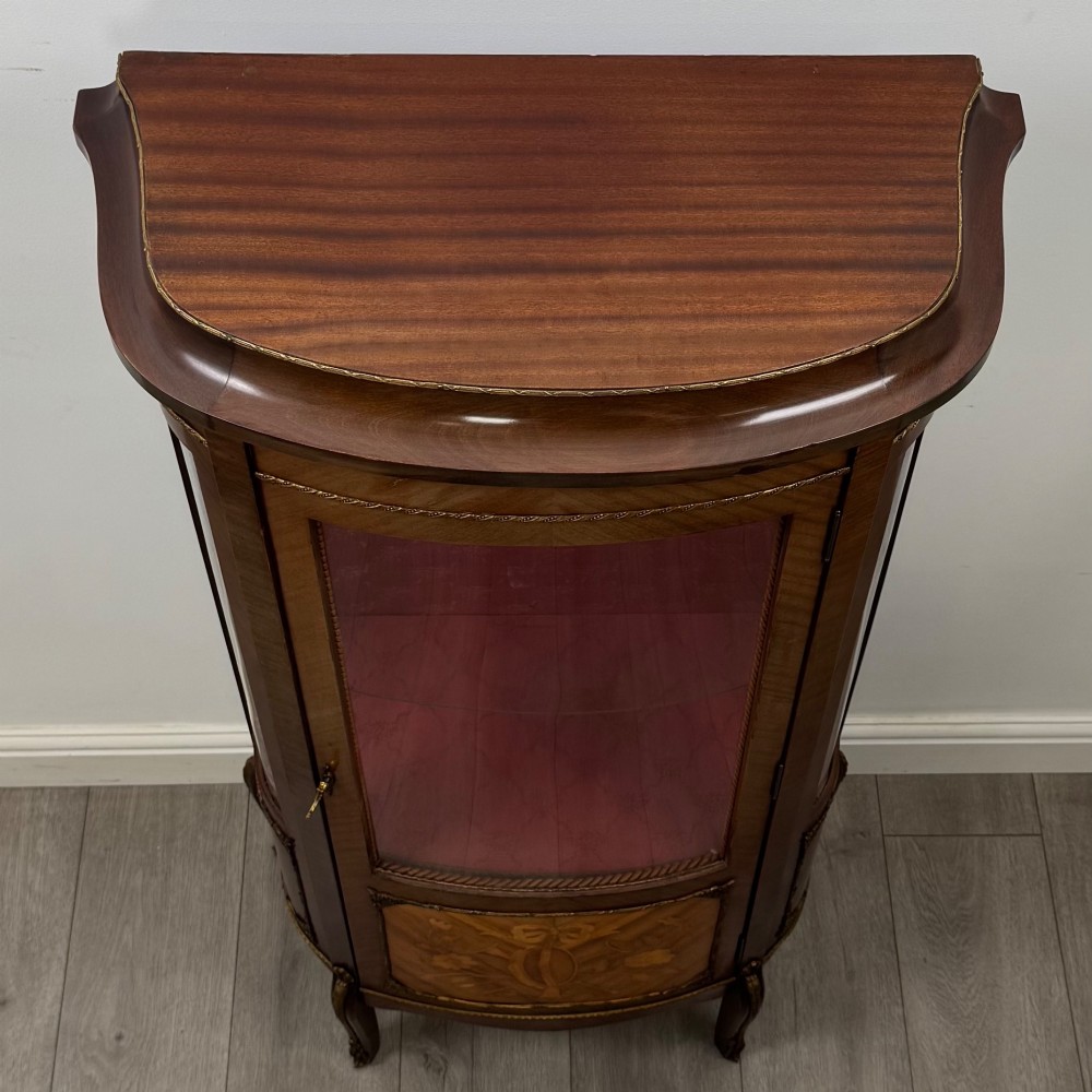 A French mahogany display vitrine featuring a curved glass door, red fabric interior lining, floral marquetry lower panel, and brass leg mounts. View X