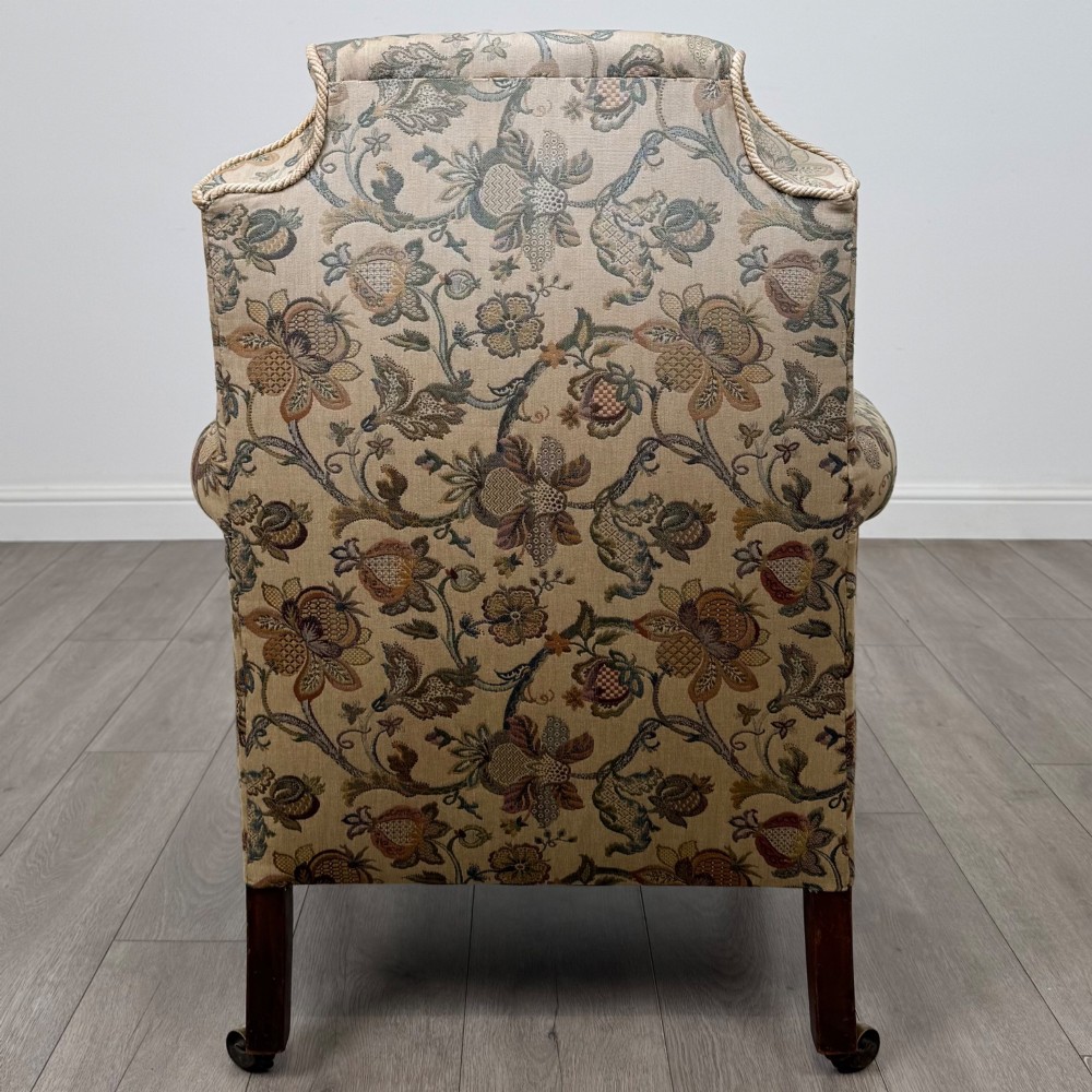 A 19th-century wingback armchair upholstered in floral tapestry fabric with turned mahogany front legs on brass castors. View IV
