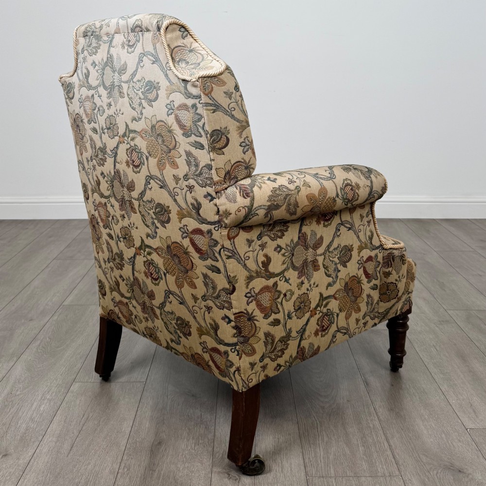 A 19th-century wingback armchair upholstered in floral tapestry fabric with turned mahogany front legs on brass castors. View V