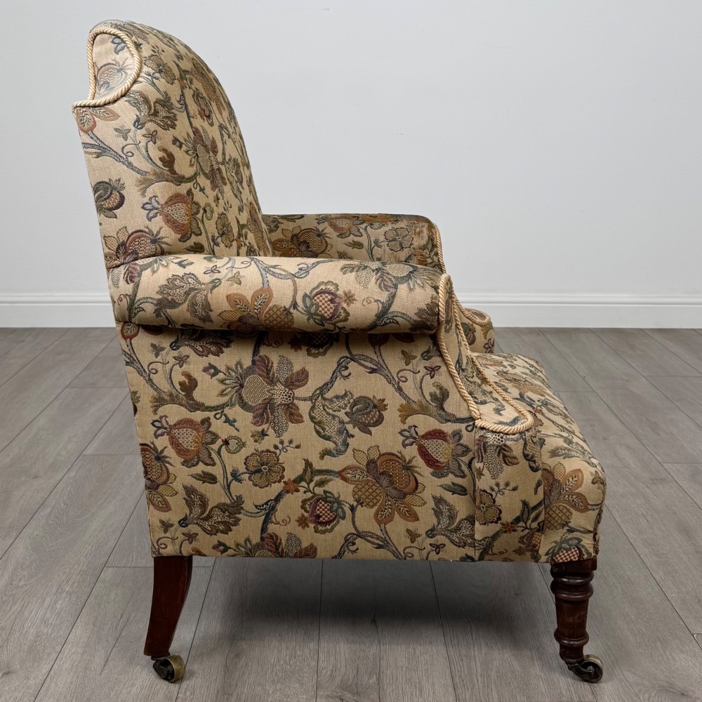 A 19th-century wingback armchair upholstered in floral tapestry fabric with turned mahogany front legs on brass castors. View VI