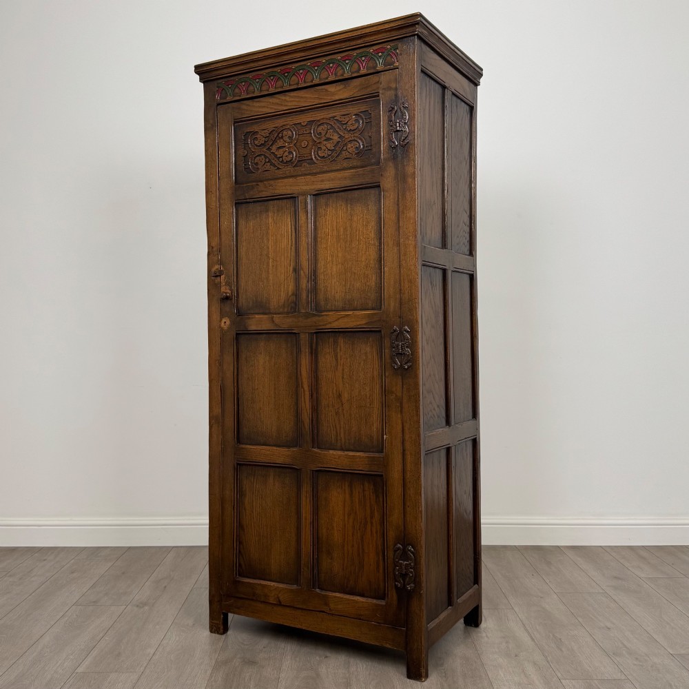A narrow twentieth-century dark oak single-door wardrobe featuring carved scrollwork panels, a decorative painted top frieze, and panelled construction. View III