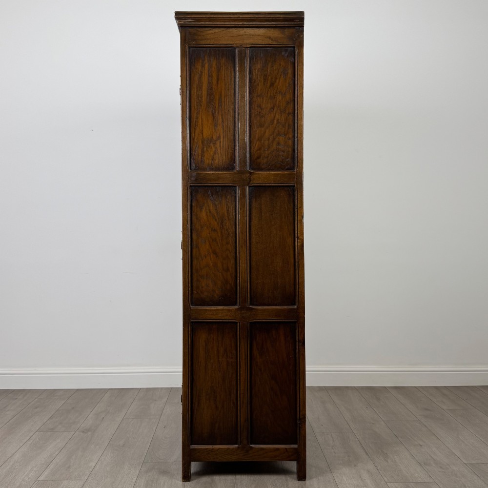 A narrow twentieth-century dark oak single-door wardrobe featuring carved scrollwork panels, a decorative painted top frieze, and panelled construction. View IV