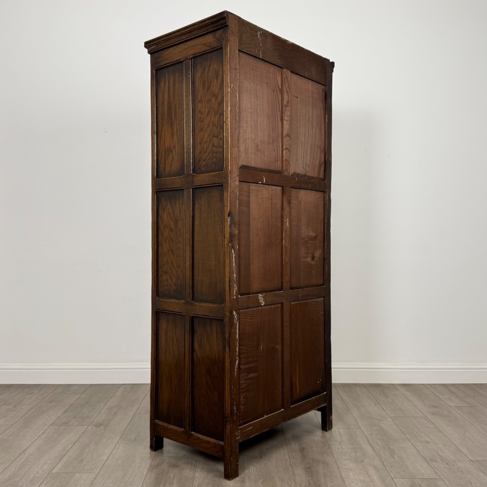 A narrow twentieth-century dark oak single-door wardrobe featuring carved scrollwork panels, a decorative painted top frieze, and panelled construction. View V