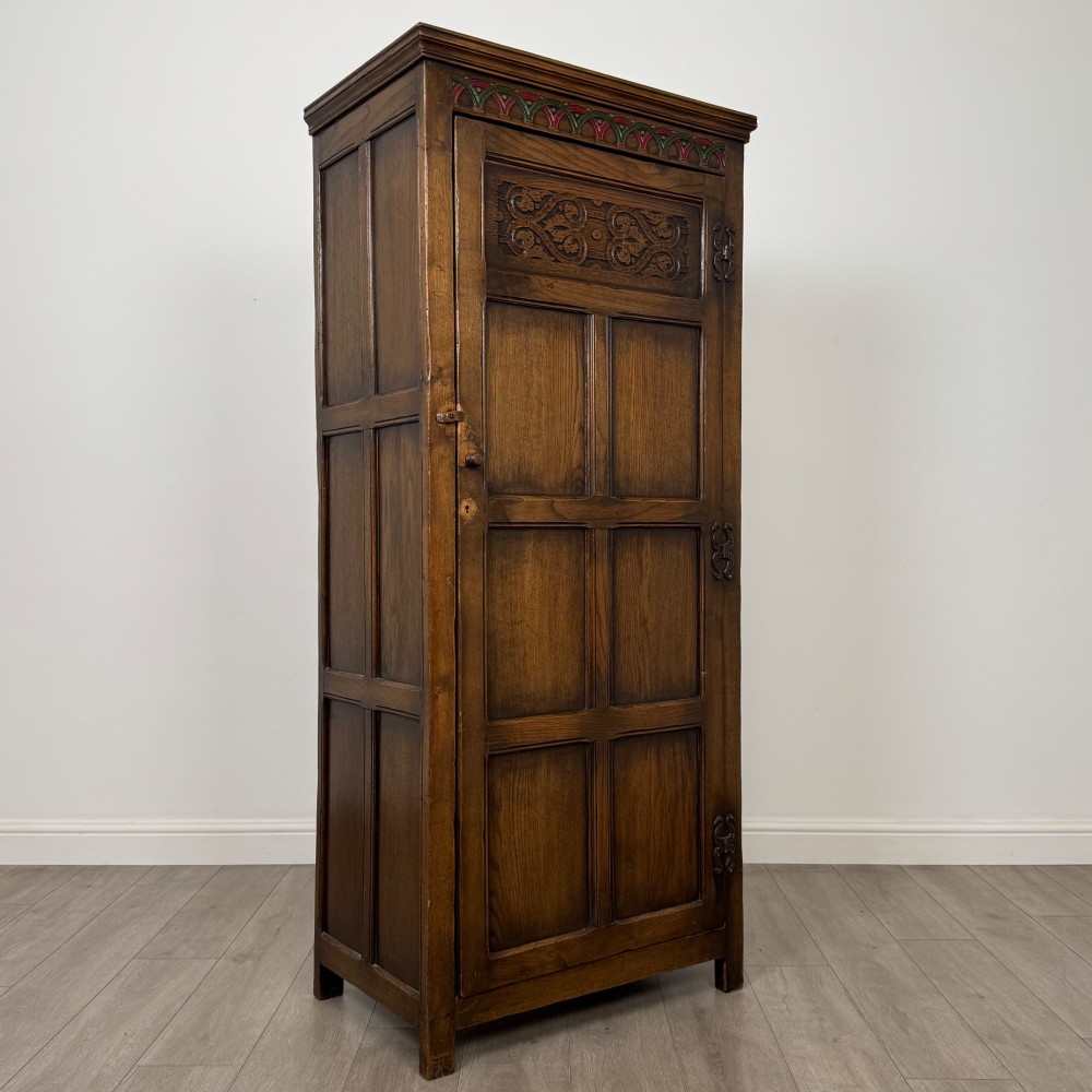 A narrow twentieth-century dark oak single-door wardrobe featuring carved scrollwork panels, a decorative painted top frieze, and panelled construction. View IX