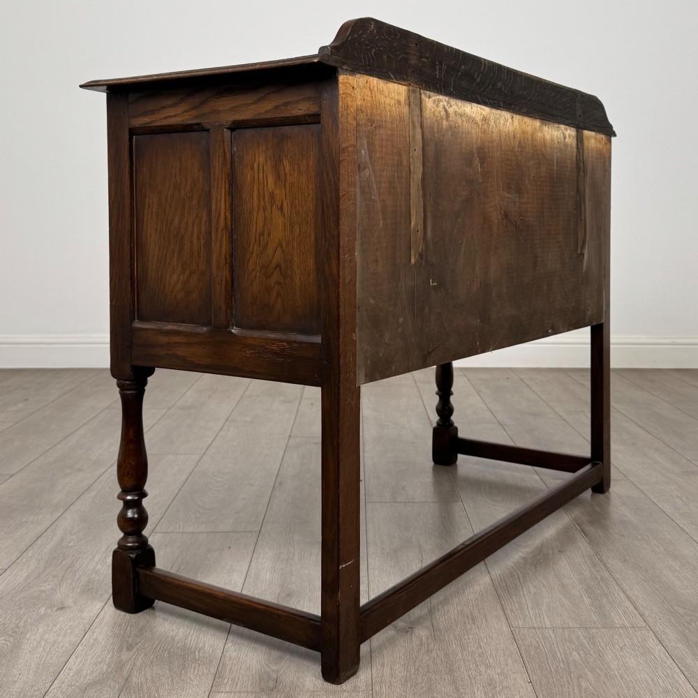 A dark oak chest featuring two top drawers above one wide bottom drawer, resting on turned legs connected by a low stretcher frame. View IV