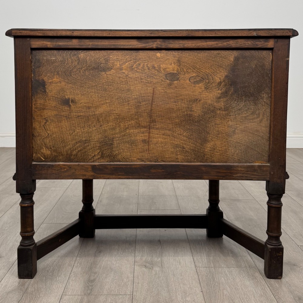 A small dark oak cupboard featuring a single carved panel door, turned legs, a lower stretcher, and decorative brass hinges. View VI