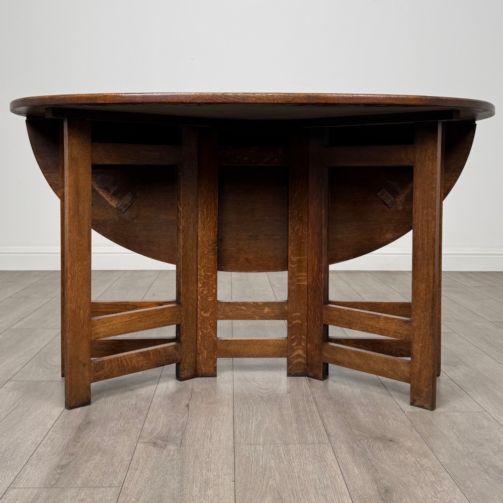 An early 20th-century Arts and Crafts solid oak gateleg table featuring drop leaves and a geometric trestle base.