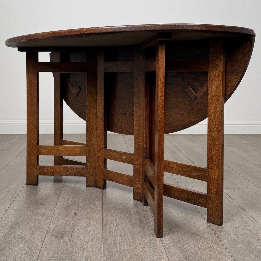 An early 20th-century Arts and Crafts solid oak gateleg table featuring drop leaves and a geometric trestle base. View II