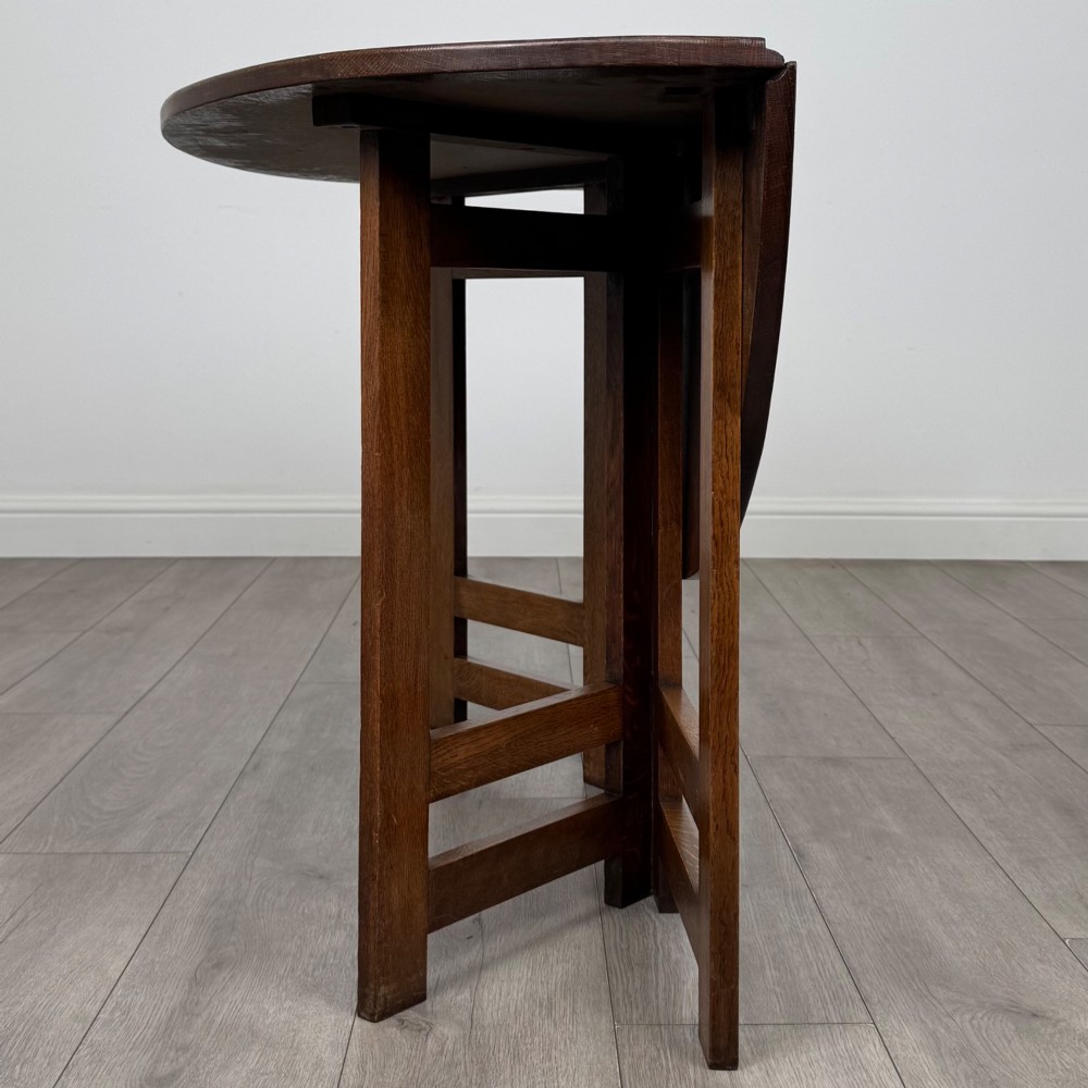 An early 20th-century Arts and Crafts solid oak gateleg table featuring drop leaves and a geometric trestle base. View III