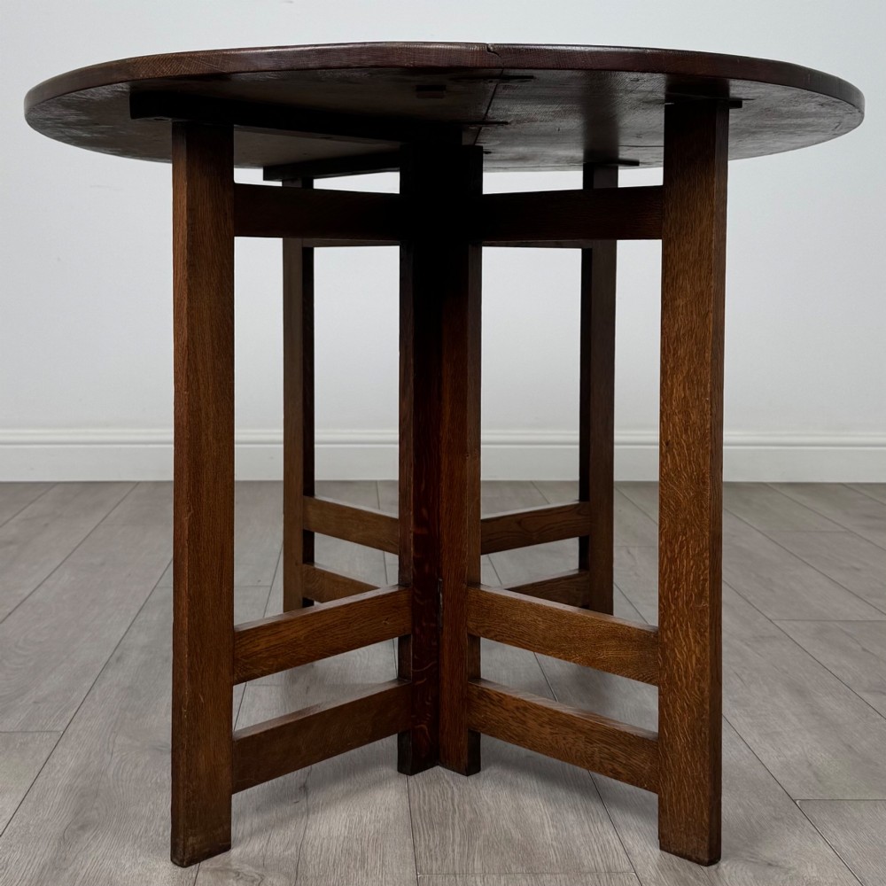 An early 20th-century Arts and Crafts solid oak gateleg table featuring drop leaves and a geometric trestle base. View IV