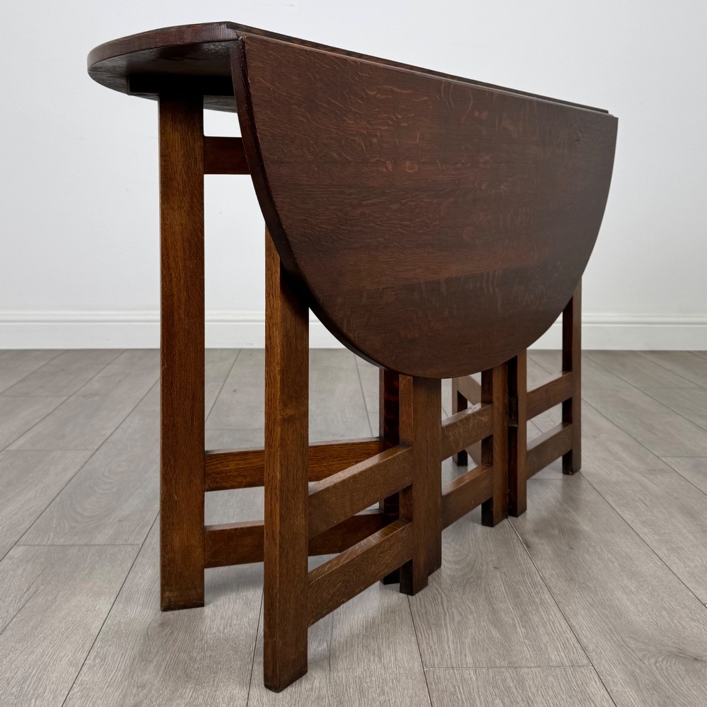 An early 20th-century Arts and Crafts solid oak gateleg table featuring drop leaves and a geometric trestle base. View V