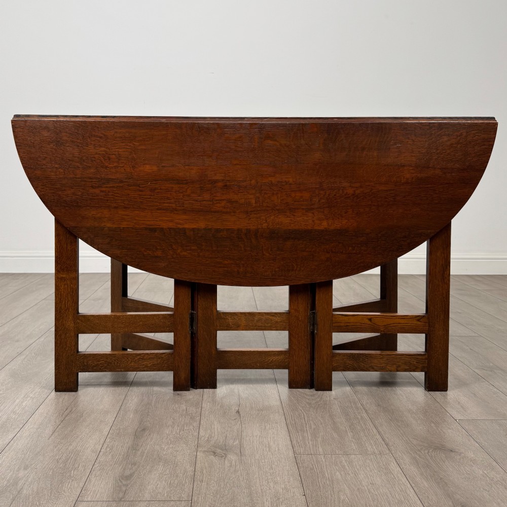 An early 20th-century Arts and Crafts solid oak gateleg table featuring drop leaves and a geometric trestle base. View VI