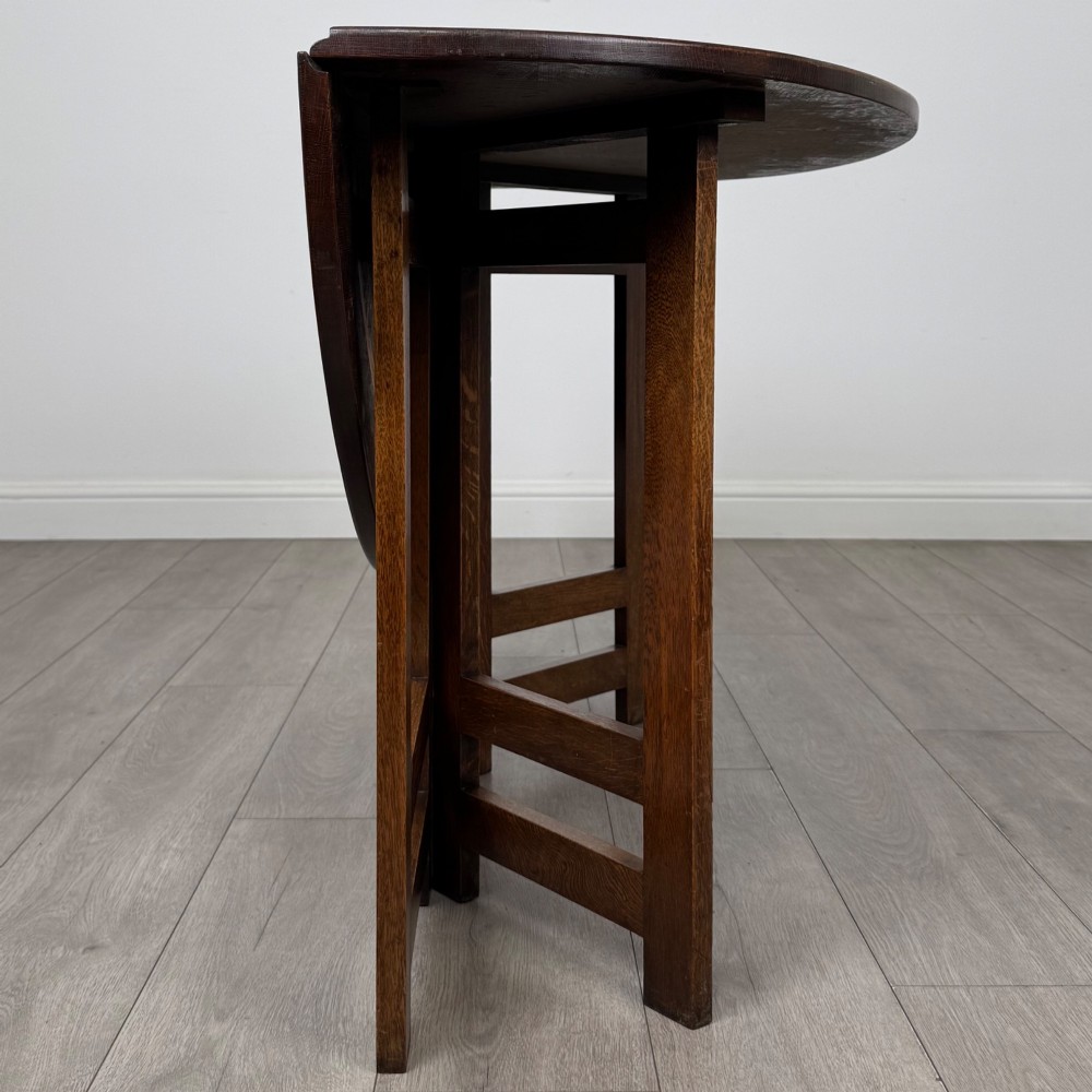 An early 20th-century Arts and Crafts solid oak gateleg table featuring drop leaves and a geometric trestle base. View VIII
