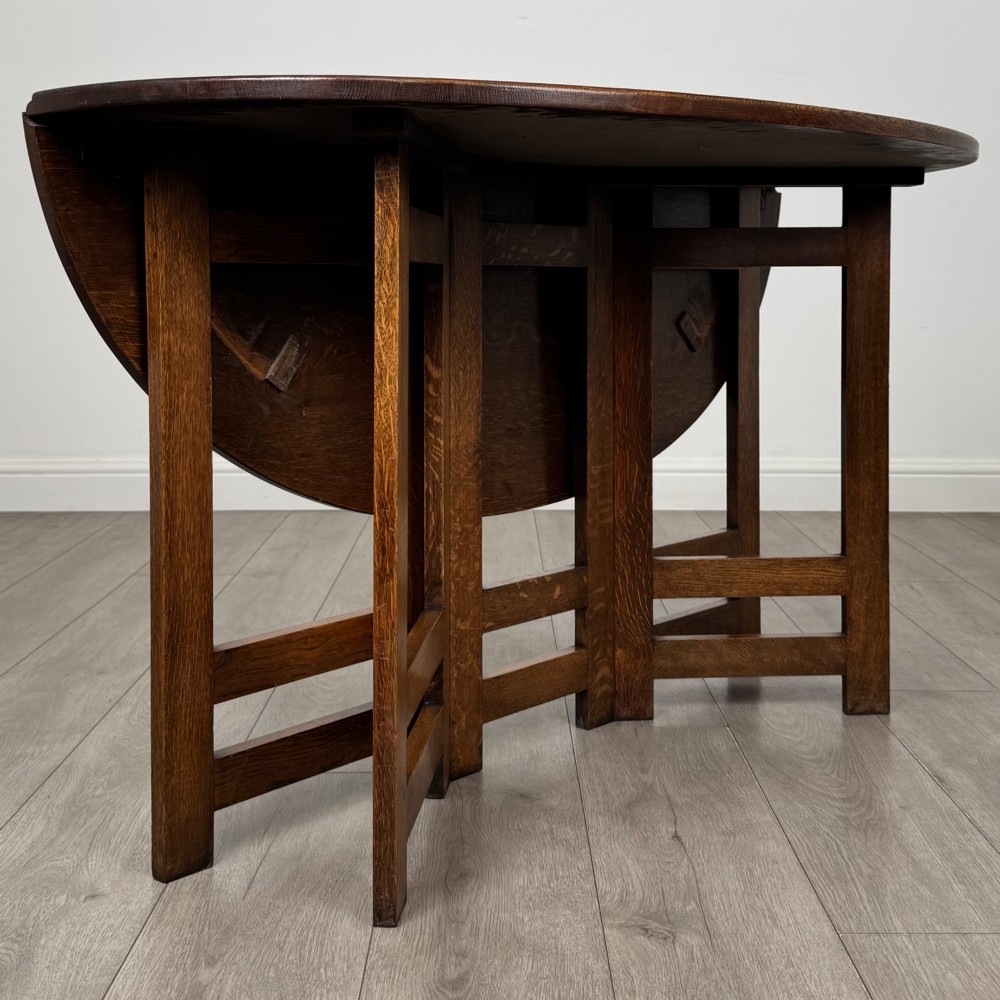 An early 20th-century Arts and Crafts solid oak gateleg table featuring drop leaves and a geometric trestle base. View IX
