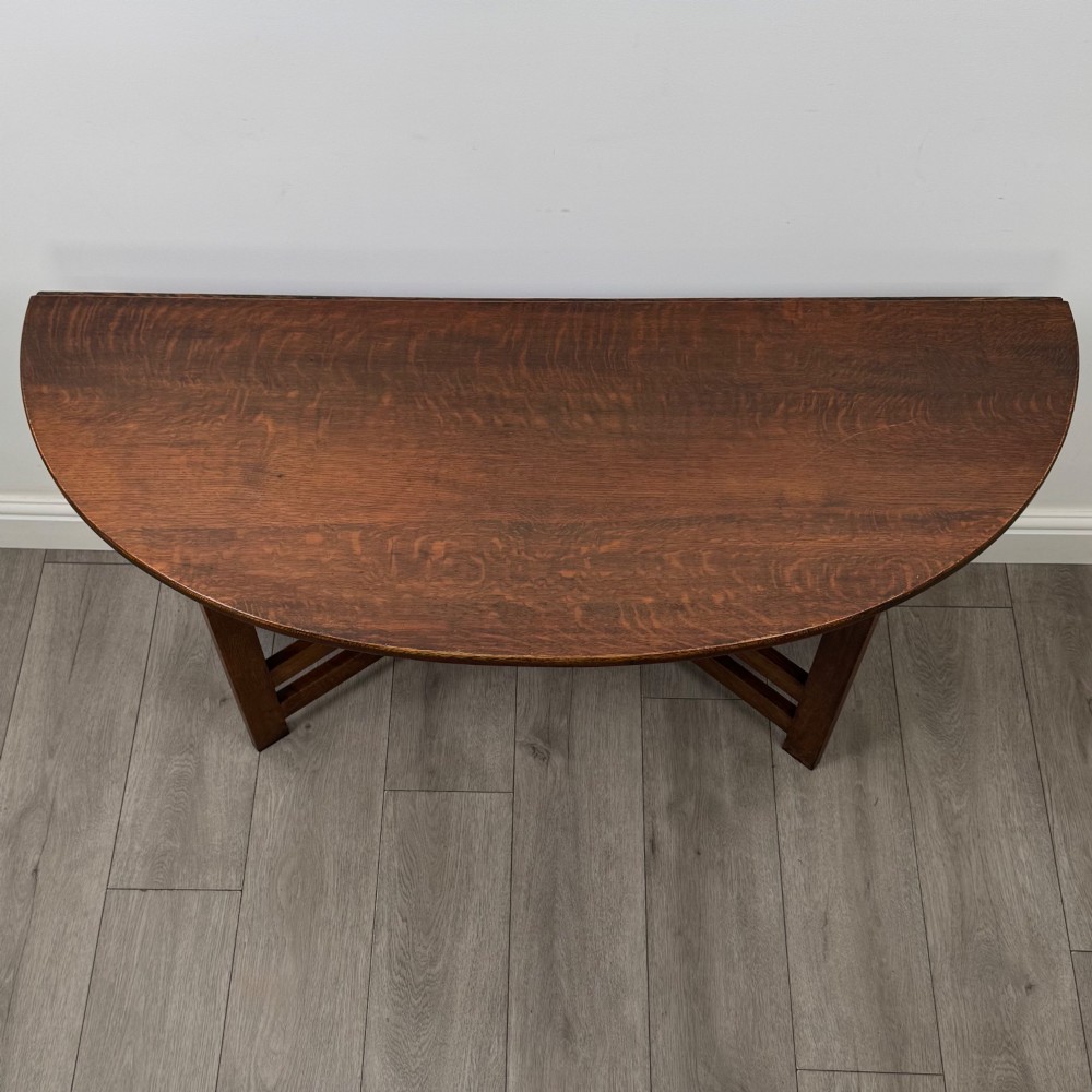 An early 20th-century Arts and Crafts solid oak gateleg table featuring drop leaves and a geometric trestle base. View X