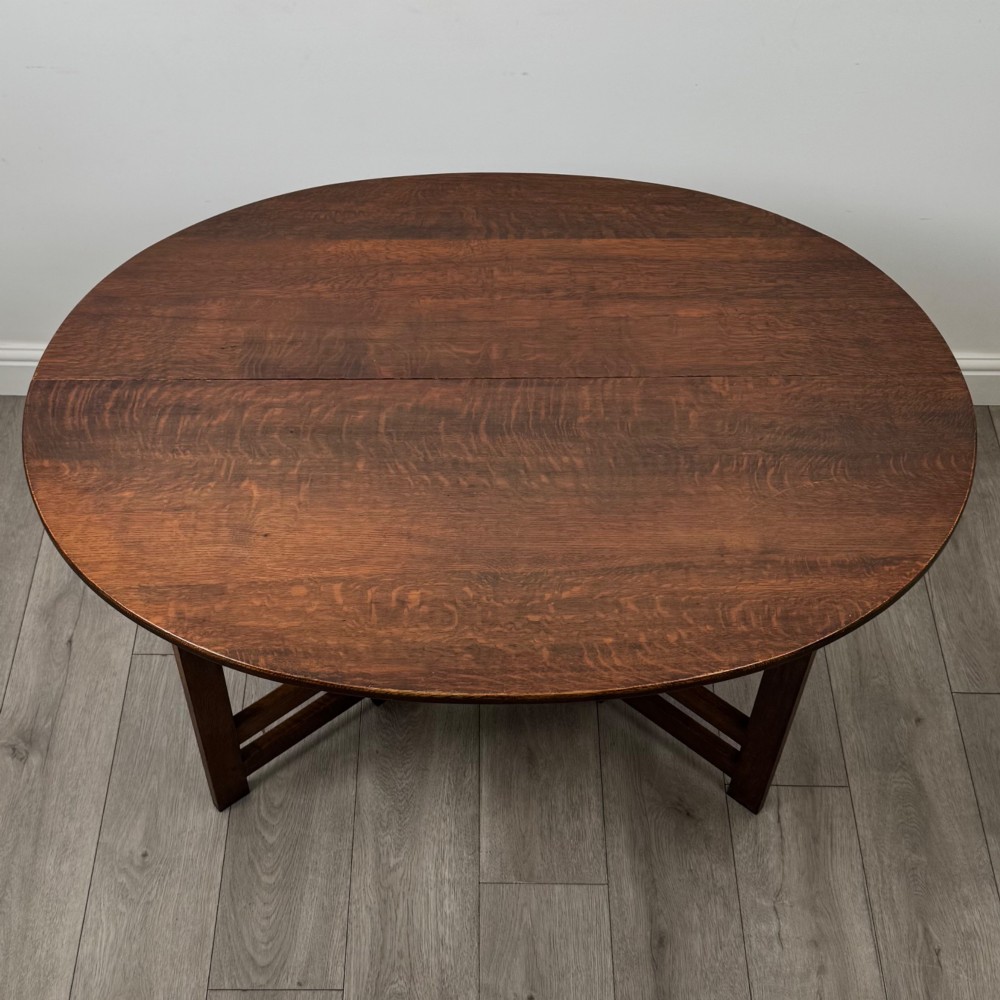 An early 20th-century Arts and Crafts solid oak gateleg table featuring drop leaves and a geometric trestle base. View XI
