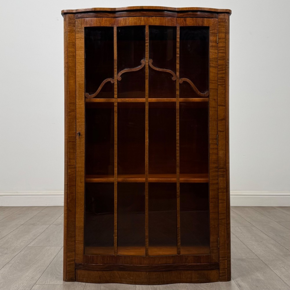 A freestanding early 20th-century display cabinet featuring figured walnut veneers, a single glazed door with decorative astragal glazing bars, and internal wooden shelves.