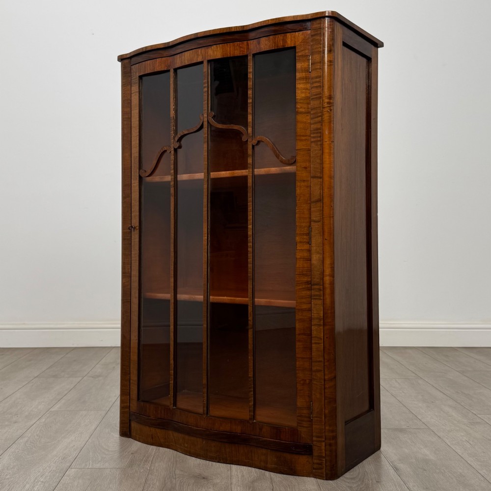 A freestanding early 20th-century display cabinet featuring figured walnut veneers, a single glazed door with decorative astragal glazing bars, and internal wooden shelves. View III