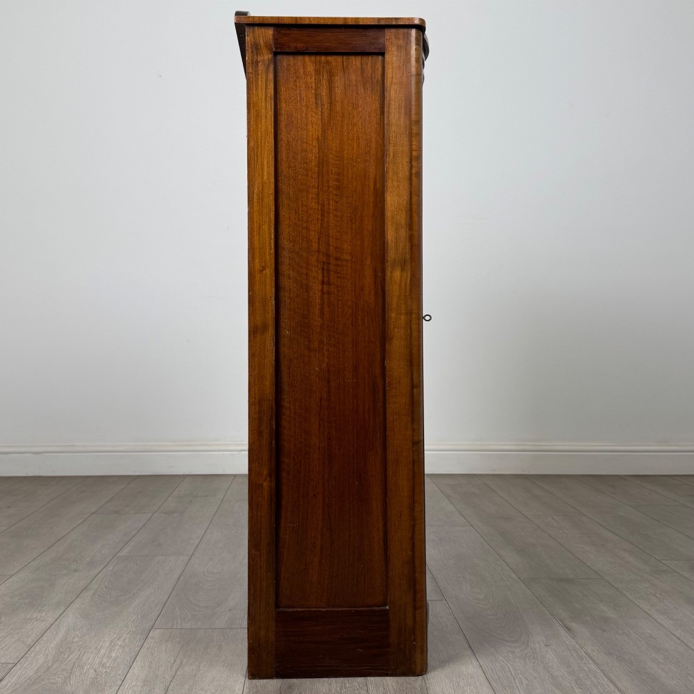 A freestanding early 20th-century display cabinet featuring figured walnut veneers, a single glazed door with decorative astragal glazing bars, and internal wooden shelves. View VIII