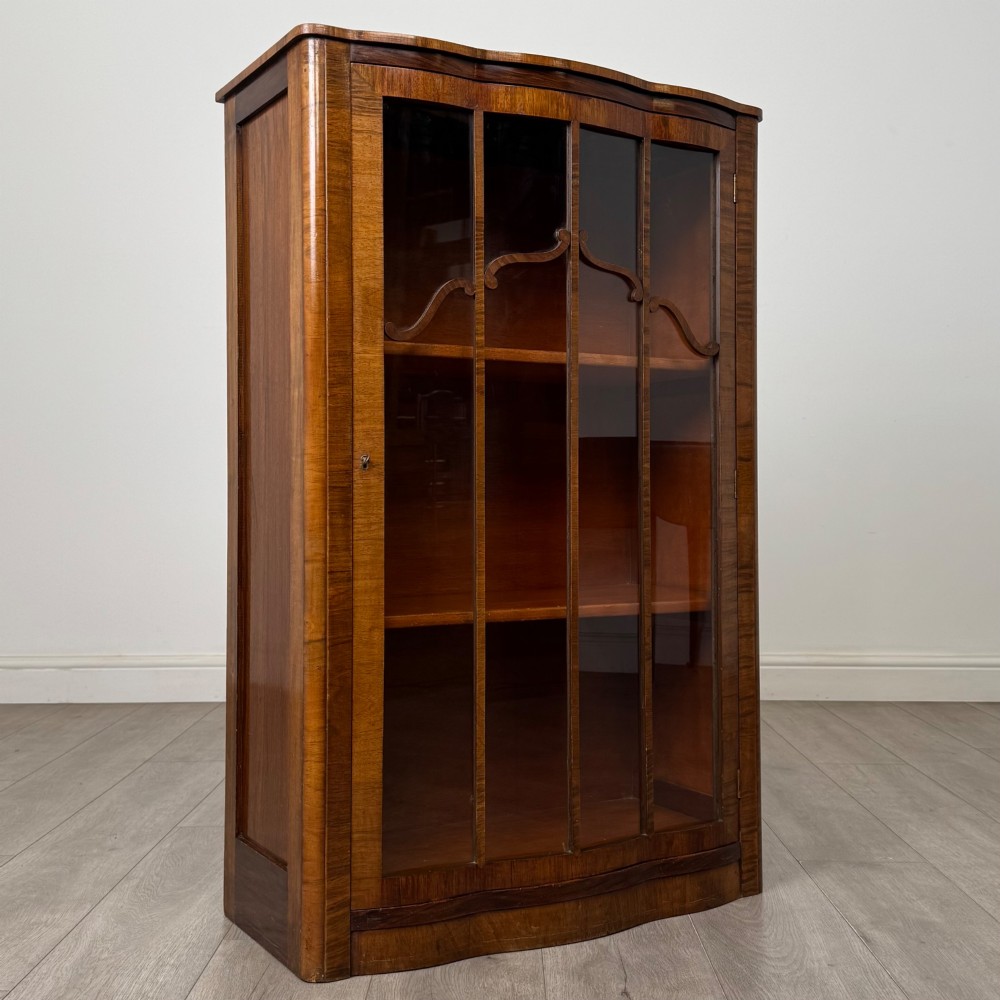 A freestanding early 20th-century display cabinet featuring figured walnut veneers, a single glazed door with decorative astragal glazing bars, and internal wooden shelves. View IX