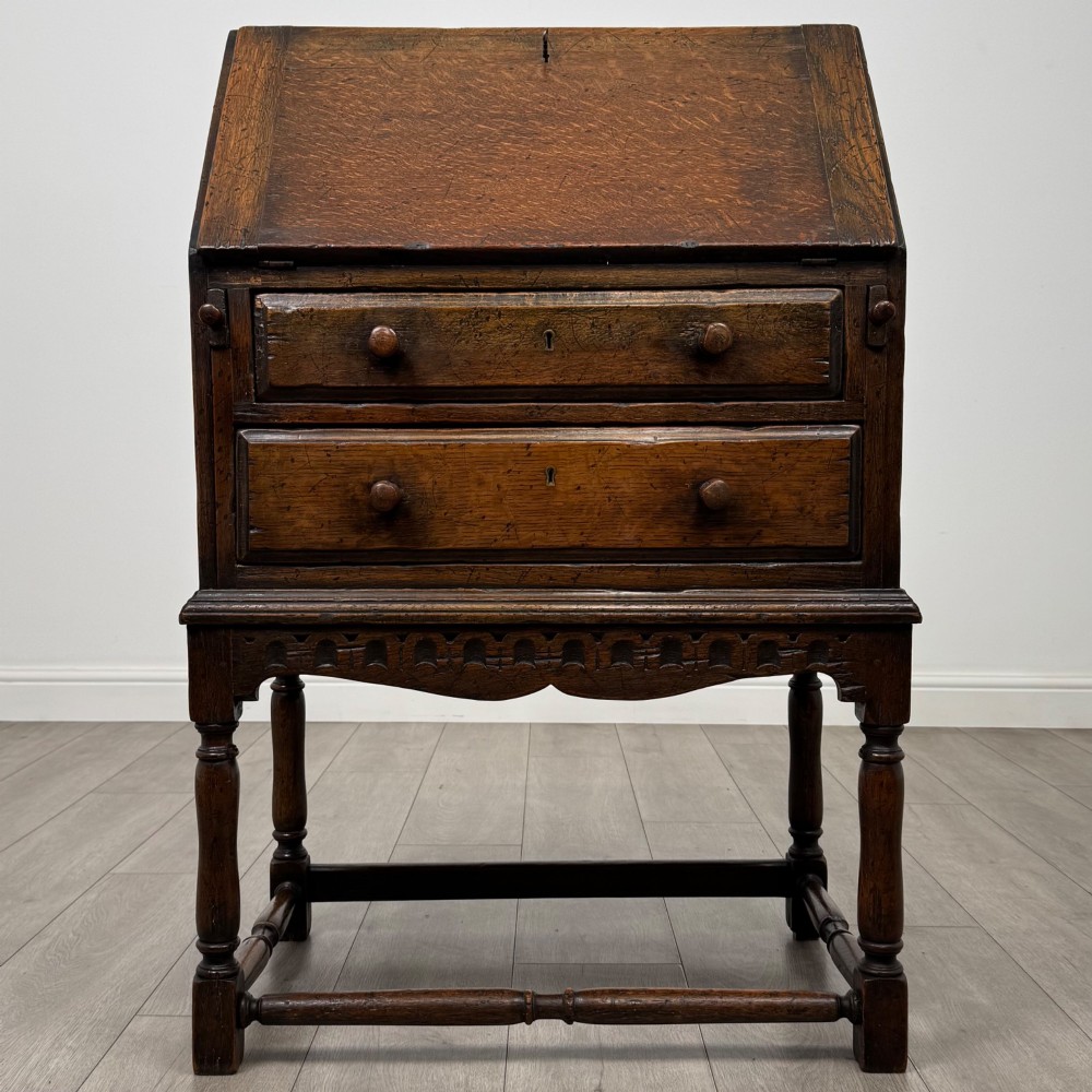 A dark oak antique bureau featuring a slanted drop-front lid above two drawers, supported by turned legs and stretchers.