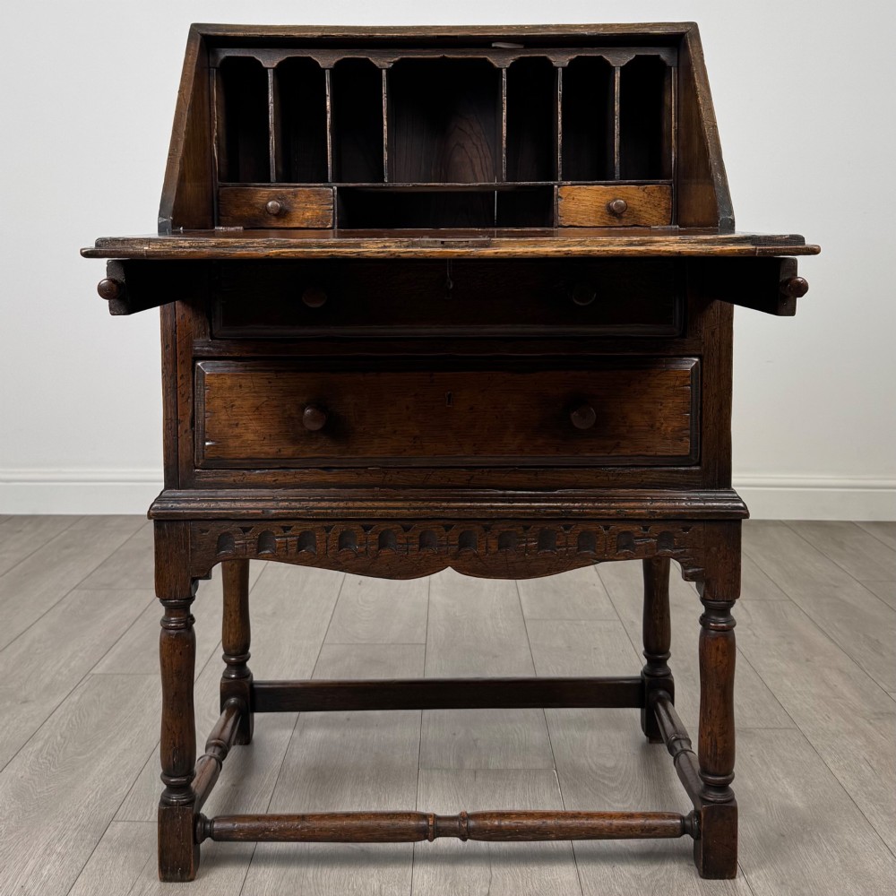 A dark oak antique bureau featuring a slanted drop-front lid above two drawers, supported by turned legs and stretchers. View II