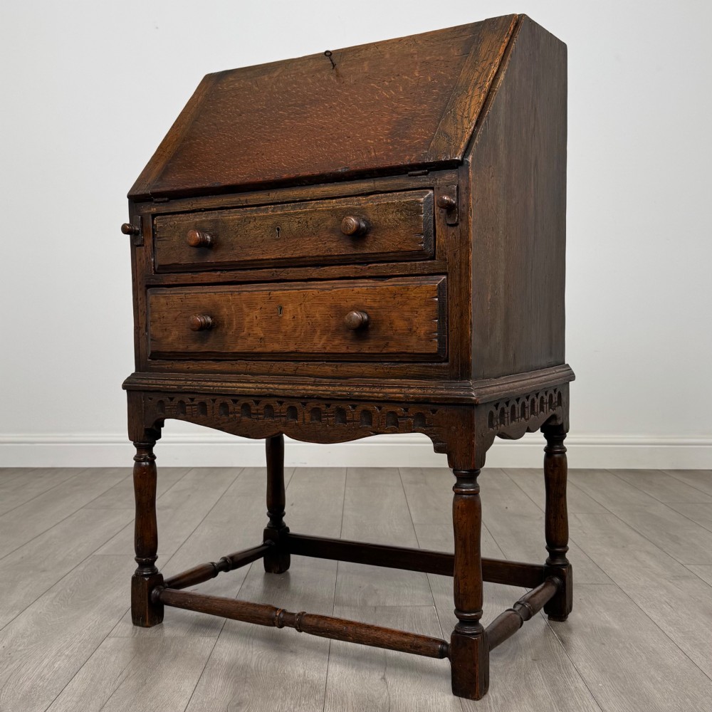 A dark oak antique bureau featuring a slanted drop-front lid above two drawers, supported by turned legs and stretchers. View III