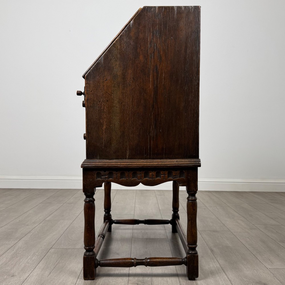 A dark oak antique bureau featuring a slanted drop-front lid above two drawers, supported by turned legs and stretchers. View IV