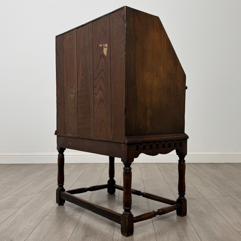 A dark oak antique bureau featuring a slanted drop-front lid above two drawers, supported by turned legs and stretchers. View VII