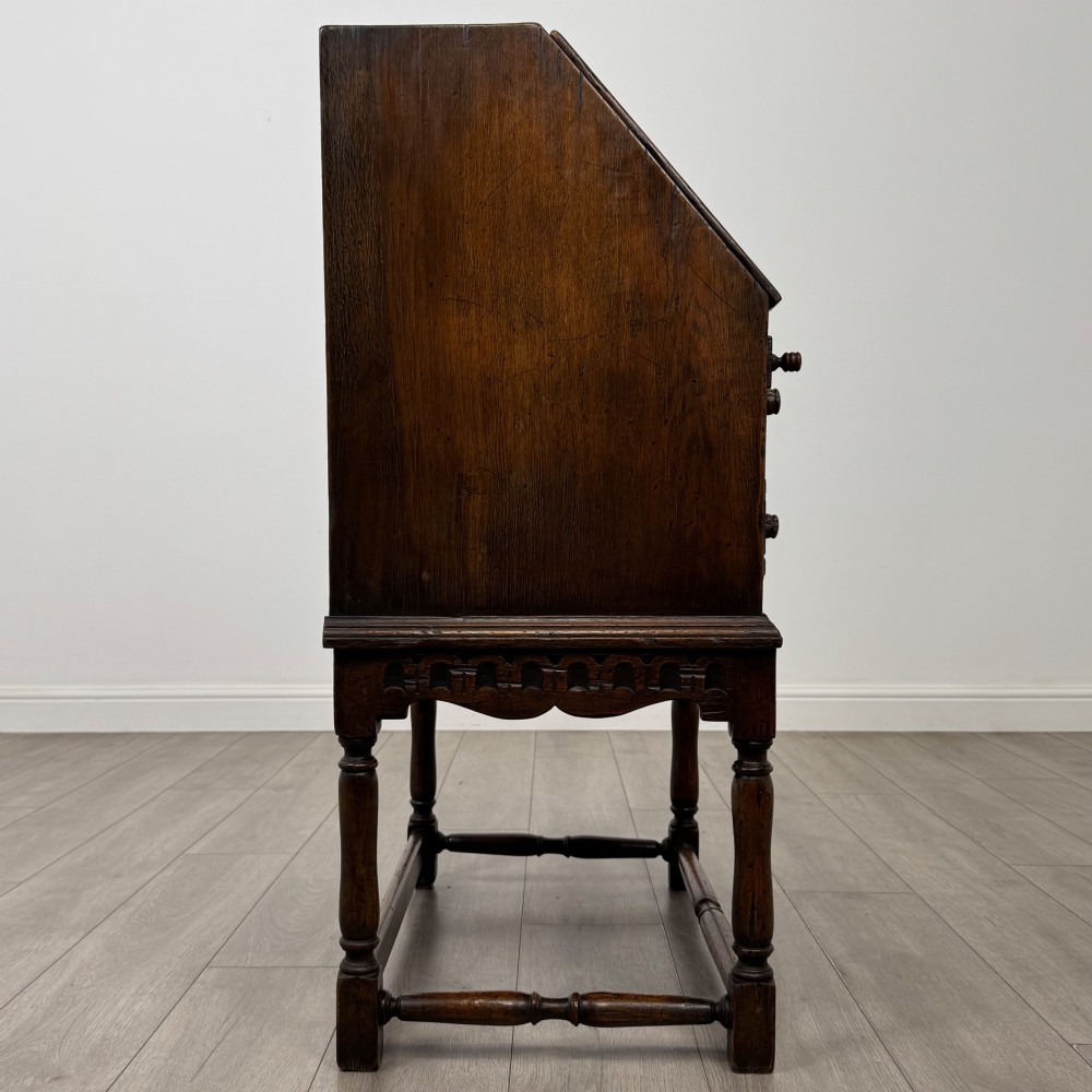 A dark oak antique bureau featuring a slanted drop-front lid above two drawers, supported by turned legs and stretchers. View VIII