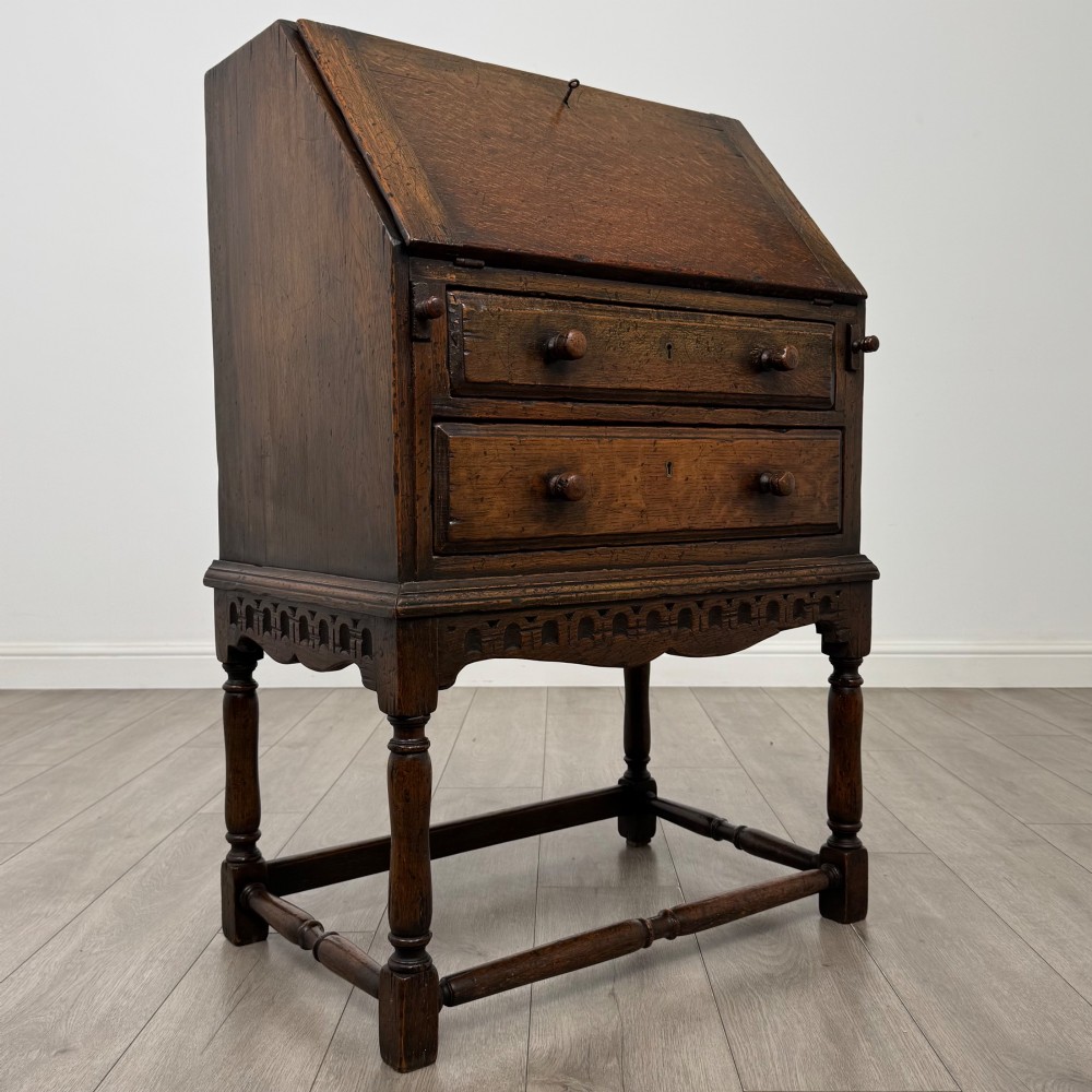 A dark oak antique bureau featuring a slanted drop-front lid above two drawers, supported by turned legs and stretchers. View IX