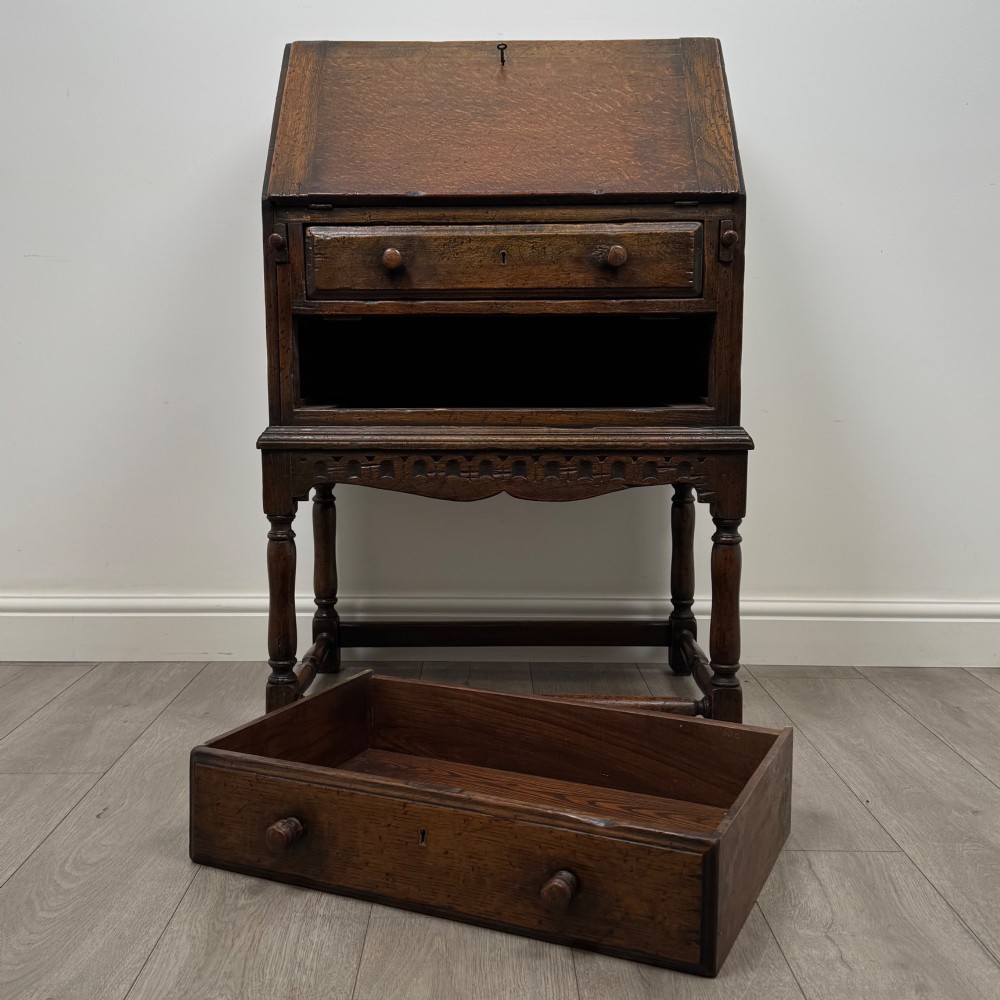 A dark oak antique bureau featuring a slanted drop-front lid above two drawers, supported by turned legs and stretchers. View XII