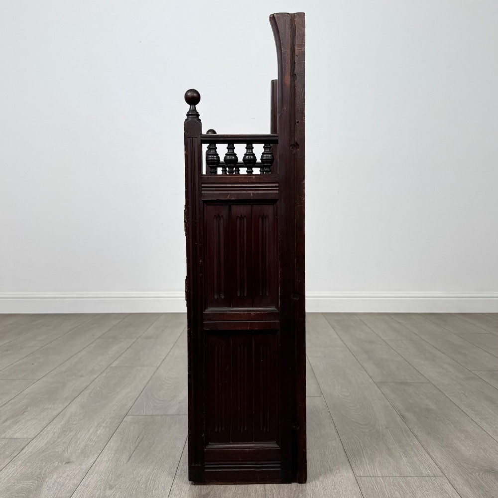 A dark mahogany hall seat cabinet featuring a carved geometric back panel, decorative brass strap hinges, double cupboard doors, and finial corner posts. View IV