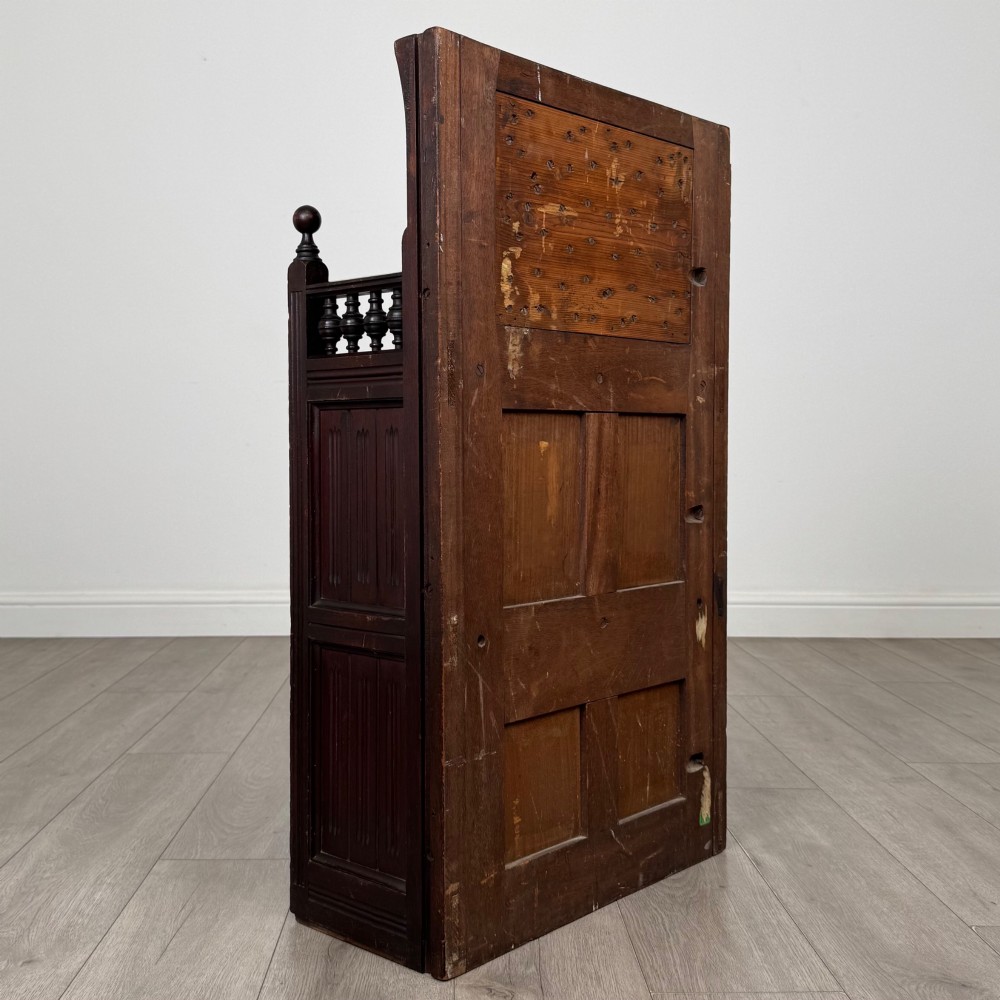 A dark mahogany hall seat cabinet featuring a carved geometric back panel, decorative brass strap hinges, double cupboard doors, and finial corner posts. View V