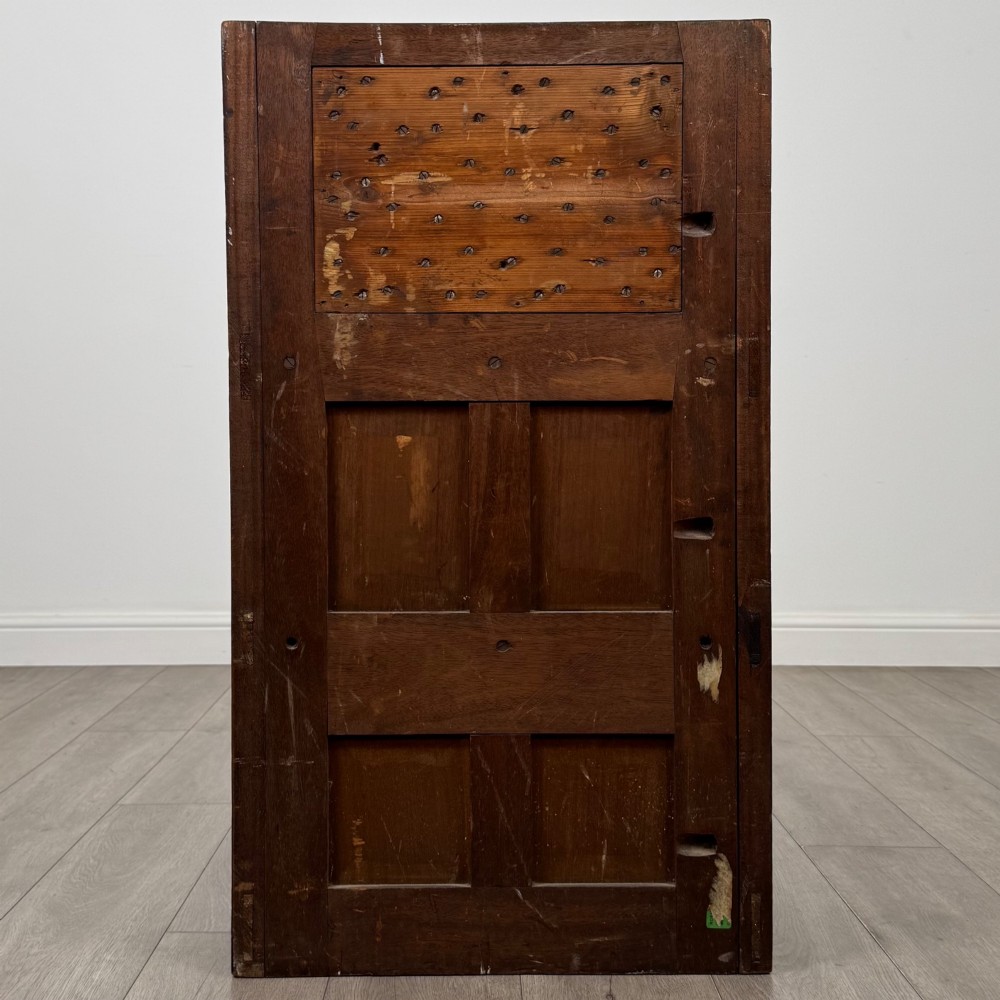 A dark mahogany hall seat cabinet featuring a carved geometric back panel, decorative brass strap hinges, double cupboard doors, and finial corner posts. View VI