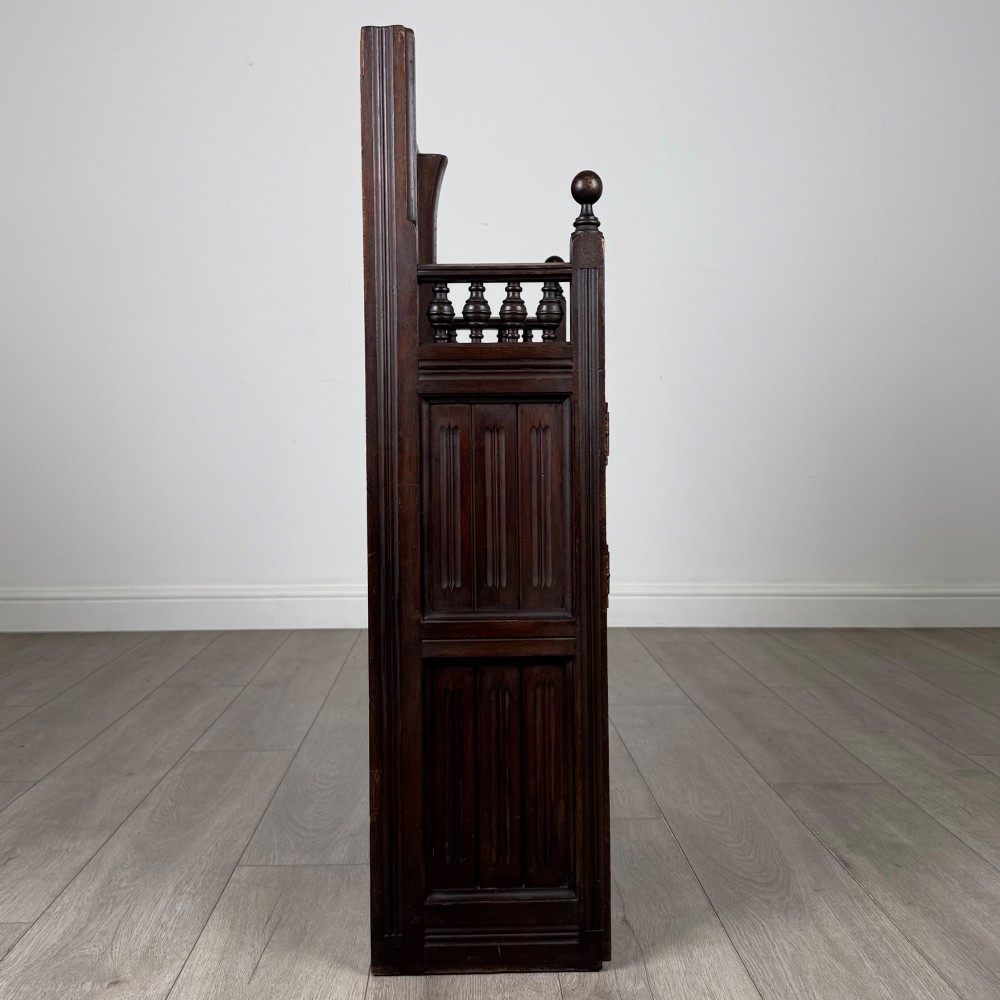 A dark mahogany hall seat cabinet featuring a carved geometric back panel, decorative brass strap hinges, double cupboard doors, and finial corner posts. View VIII
