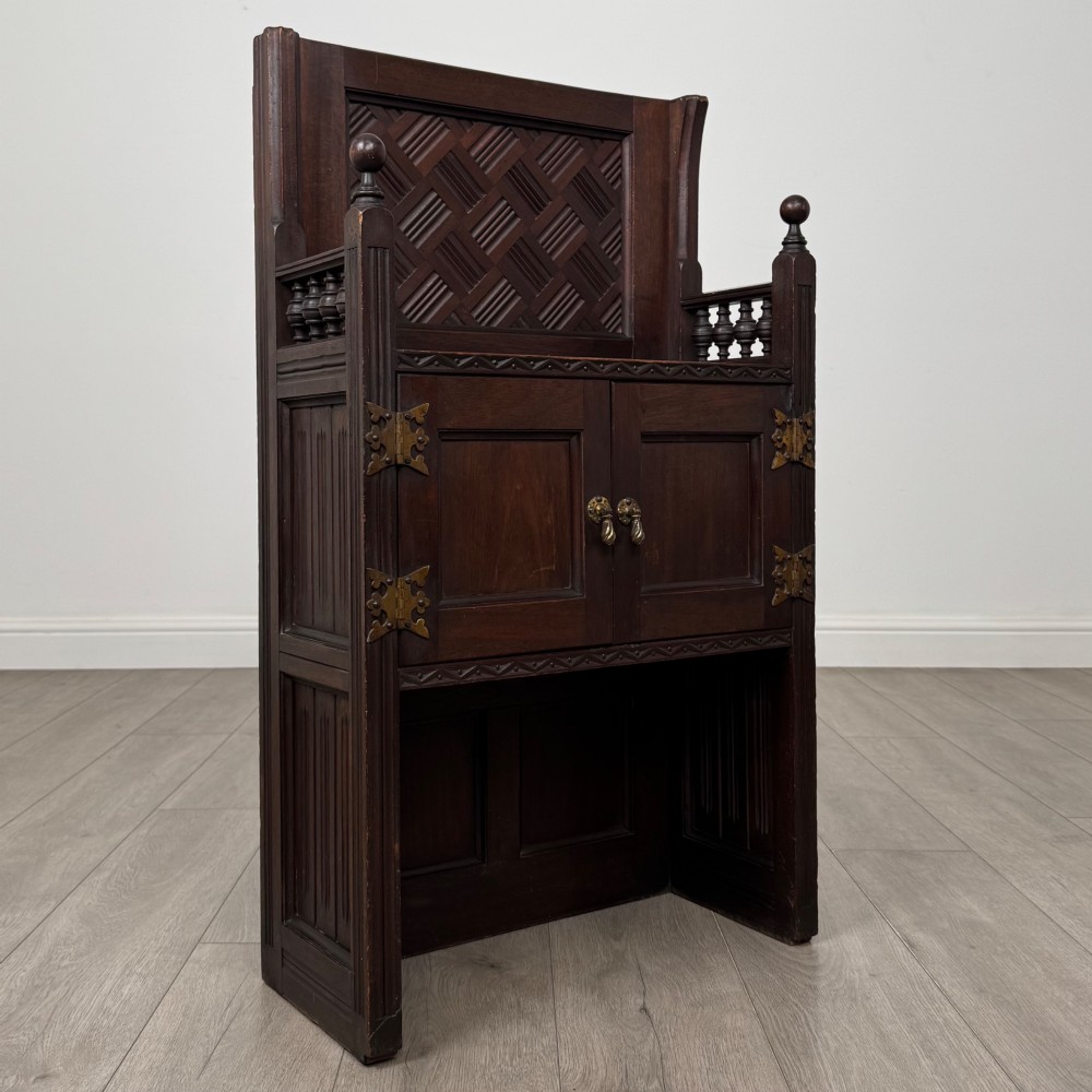 A dark mahogany hall seat cabinet featuring a carved geometric back panel, decorative brass strap hinges, double cupboard doors, and finial corner posts. View IX