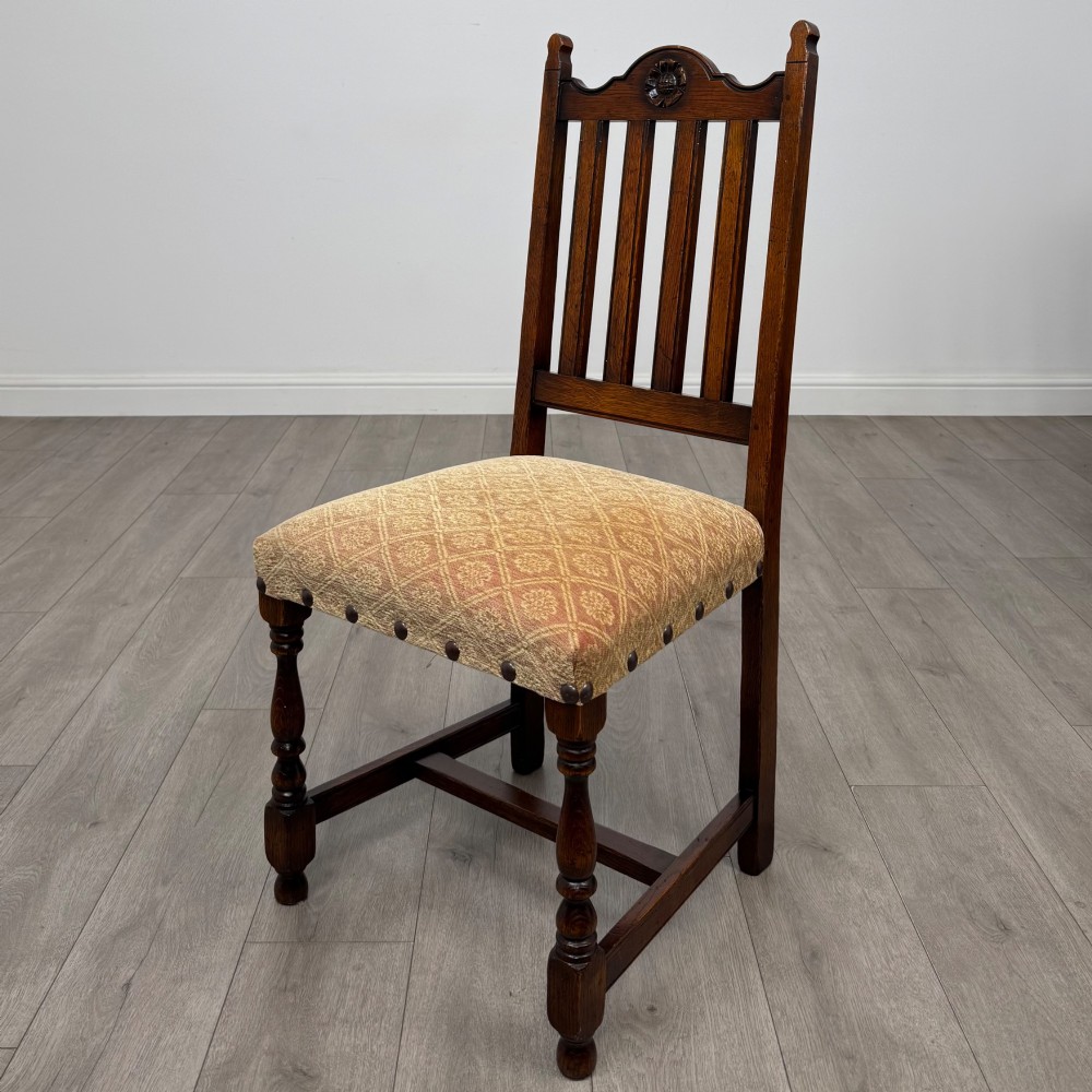 A set of six dark oak dining chairs including two armchairs and four side chairs, featuring slat backs with carved crest details and patterned fabric seats. View III