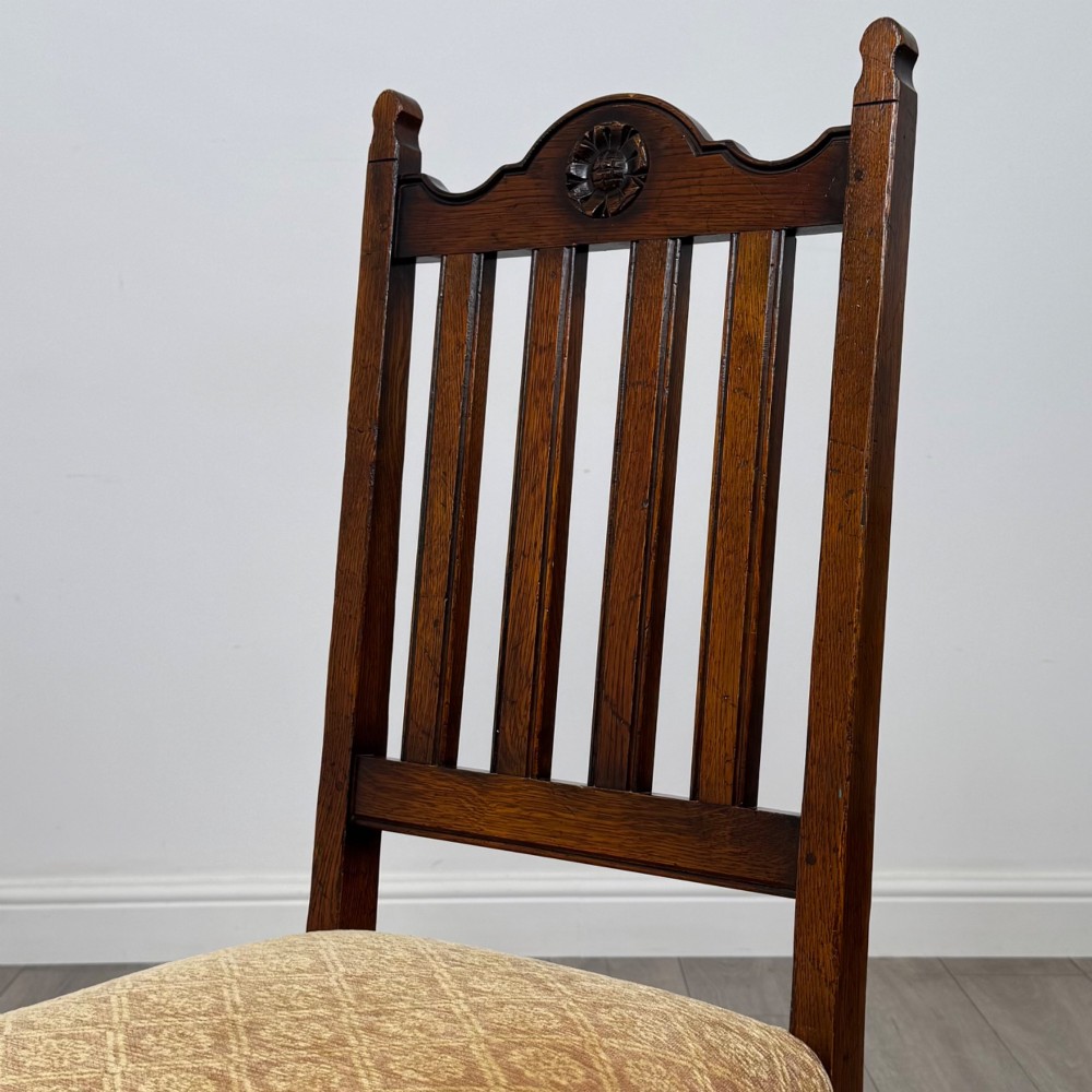 A set of six dark oak dining chairs including two armchairs and four side chairs, featuring slat backs with carved crest details and patterned fabric seats. View V