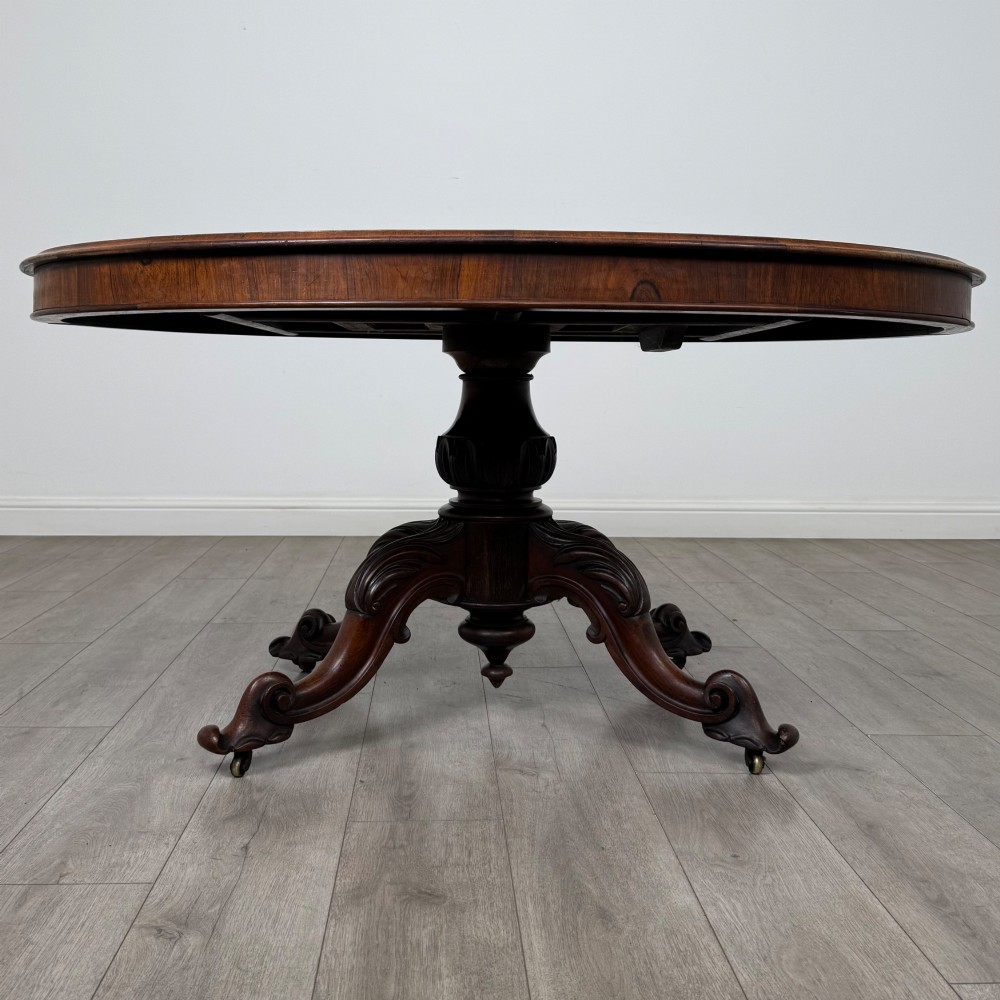 A 19th-century Victorian circular rosewood breakfast table with a carved central pedestal column and four scroll legs with brass castors.