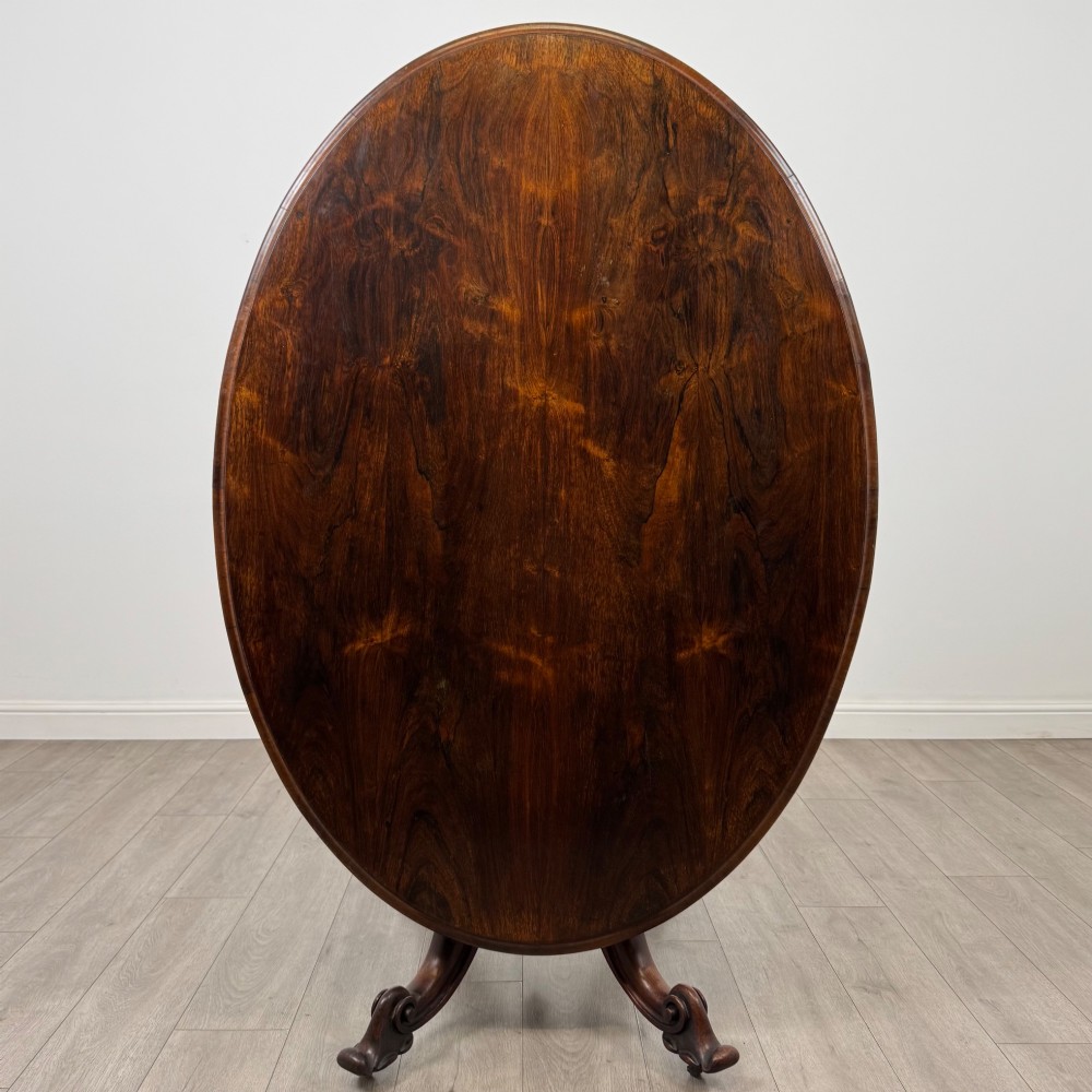 A 19th-century Victorian circular rosewood breakfast table with a carved central pedestal column and four scroll legs with brass castors. View III