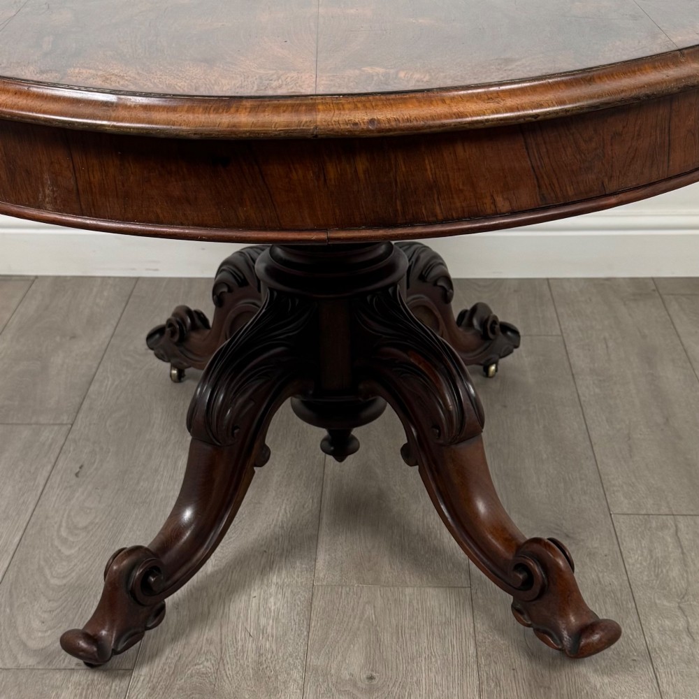 A 19th-century Victorian circular rosewood breakfast table with a carved central pedestal column and four scroll legs with brass castors. View V