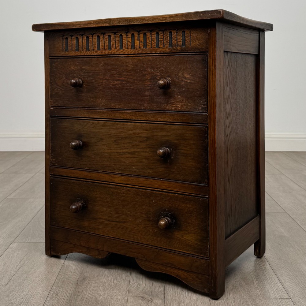 A small early twentieth-century dark oak chest of drawers featuring three drawers with turned wooden knobs and a carved frieze top detail. View II