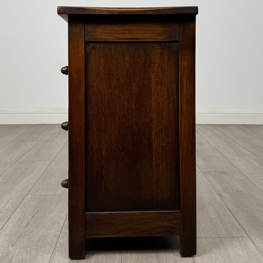 A small early twentieth-century dark oak chest of drawers featuring three drawers with turned wooden knobs and a carved frieze top detail. View III